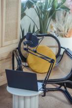 Zdjęcie przedstawia niewielki stolik, do którego jest przytwierdzony mikrofon radiowy. Na stoliku stoi laptop. W tle widać fotel z żółtą poduszką.